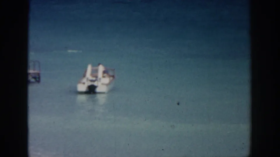 Rhodes 1962 8mm frame with a small white motorboat on blue-green sea and part of a dock at the left edge.