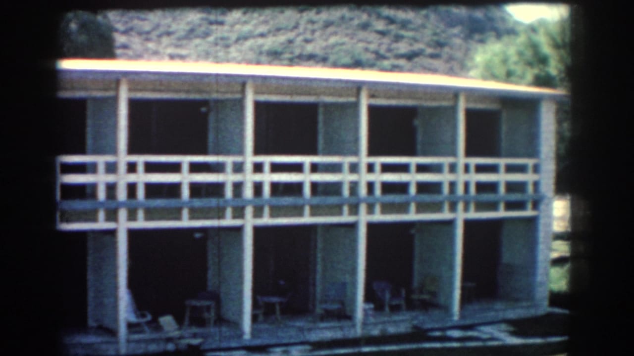 Two-story building facade with balcony, columns, dark doorways, and trees at the edge.