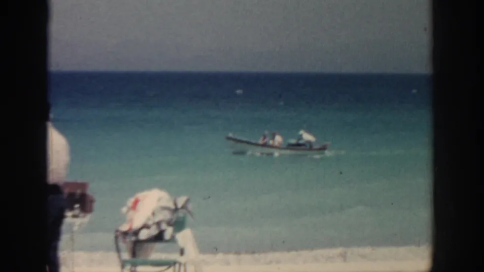 Small boat on the water off a Rhodes beach, with folding chairs and beach items visible in the foreground.