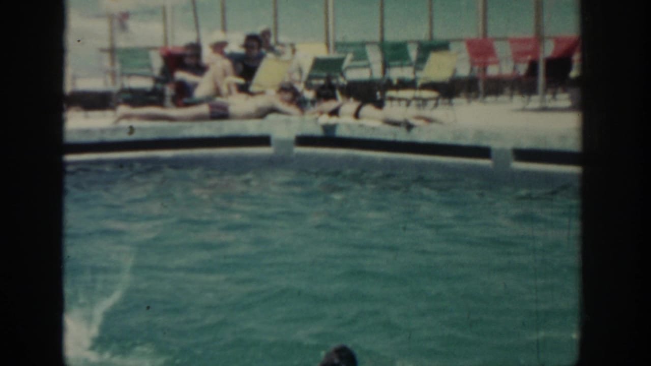 1962 Rhodes resort pool scene with swimmers in turquoise water and adults relaxing on lounge chairs in the background.
