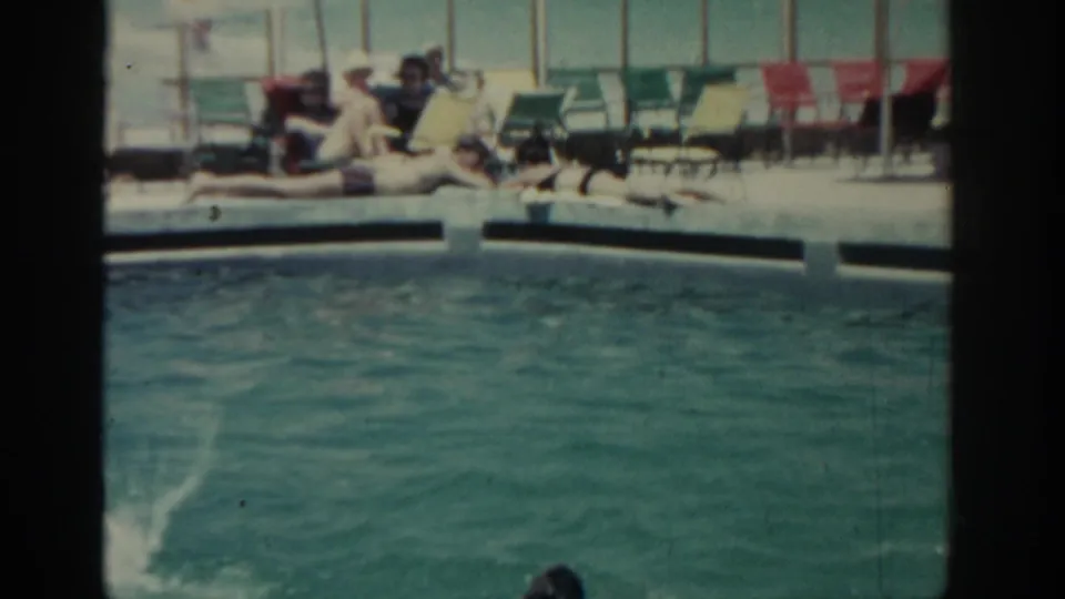 1962 Rhodes resort pool scene with swimmers in turquoise water and adults relaxing on lounge chairs in the background.