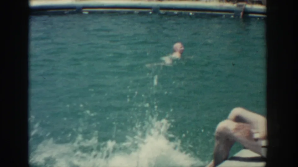 A splash spreads across the Rhodes pool after the woman jumps in, with other adult swimmers visible in the water.