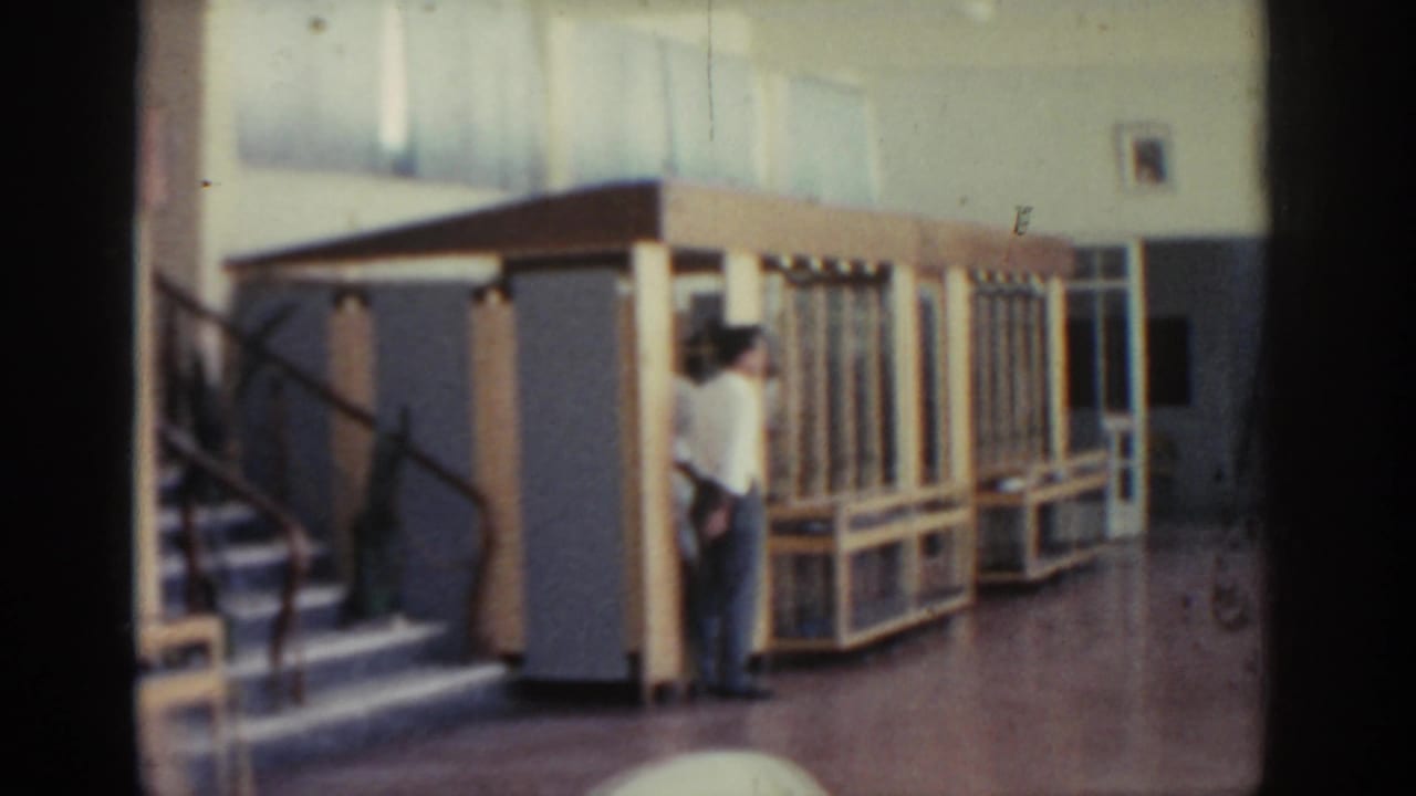 Museum interior in Rhodes, Greece, with a man near a wooden case, a stairway, and metal railing visible in soft 8mm focus.