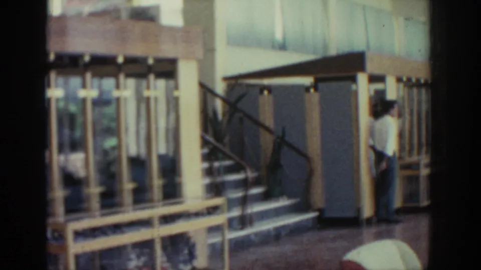Soft 8mm view of glass-fronted wooden exhibition cases, with a staircase and man partly visible in the museum interior.