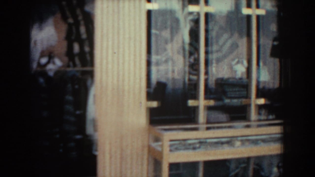 1962 Rhodes home-movie frame showing a close view of a wood-framed window with glass reflections and shadowed interior details.