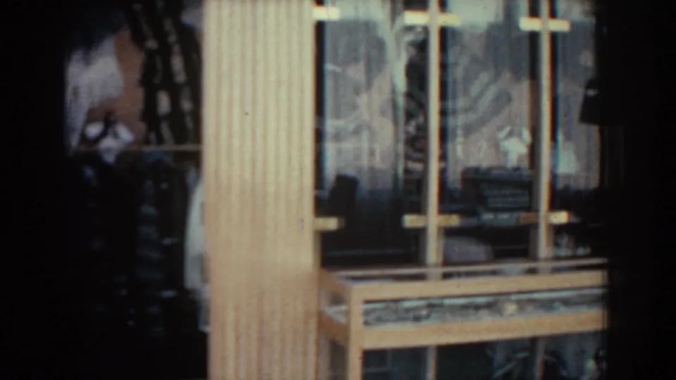 1962 Rhodes home-movie frame showing a close view of a wood-framed window with glass reflections and shadowed interior details.