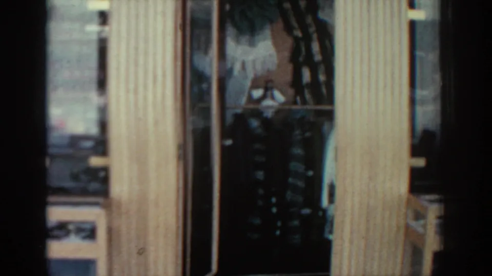 1962 Rhodes frame with pale wood trim, window panes, and a dark interior area where hanging fabric or clothing appears visible.