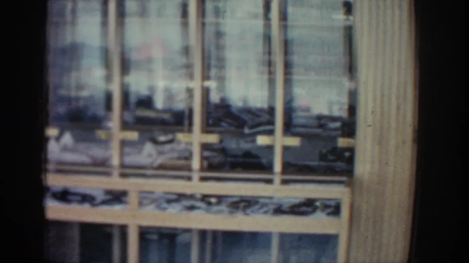 Final 1962 Rhodes frame showing a close-up window grid, pale wooden trim, reflected daylight, and indistinct interior objects.