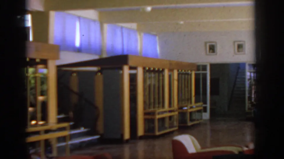 1962 Rhodes hotel interior showing wood-and-glass display cases, blue curtains, a stairway, and polished flooring.