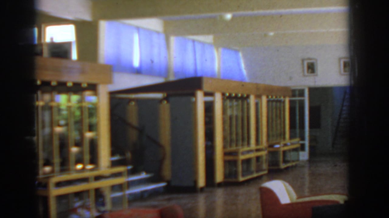 Well-lit interior with wooden glass display cases, high windows, polished floor, and red chair.