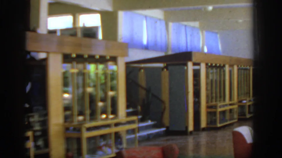 1962 Rhodes interior view with wooden display cases, glass panels, a dark stair rail, high windows, and red upholstered seating in the foreground.