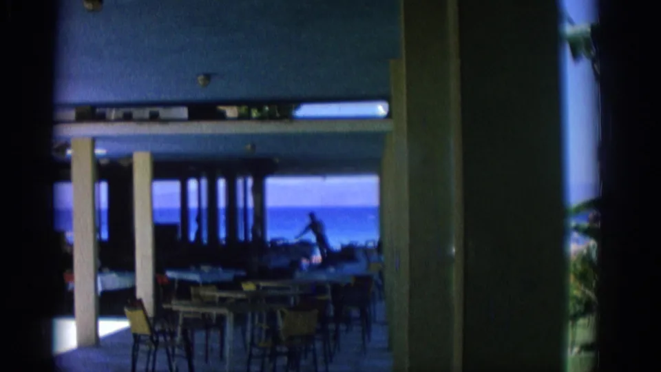 Open-air beachfront dining area in Rhodes with tables and chairs silhouetted against blue sea and sky beyond the shaded interior.