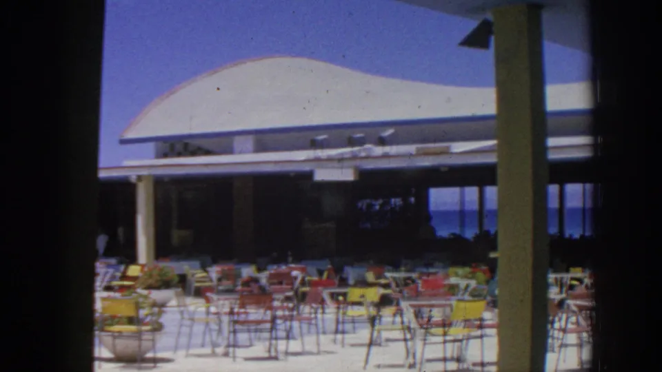 Rhodes, Greece, 1962 home-movie frame of an outdoor restaurant terrace with vivid chairs and sea-facing openings.