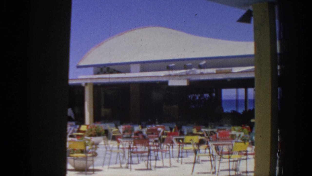 Outdoor resort dining area with colorful chairs and tables beneath a white canopy.