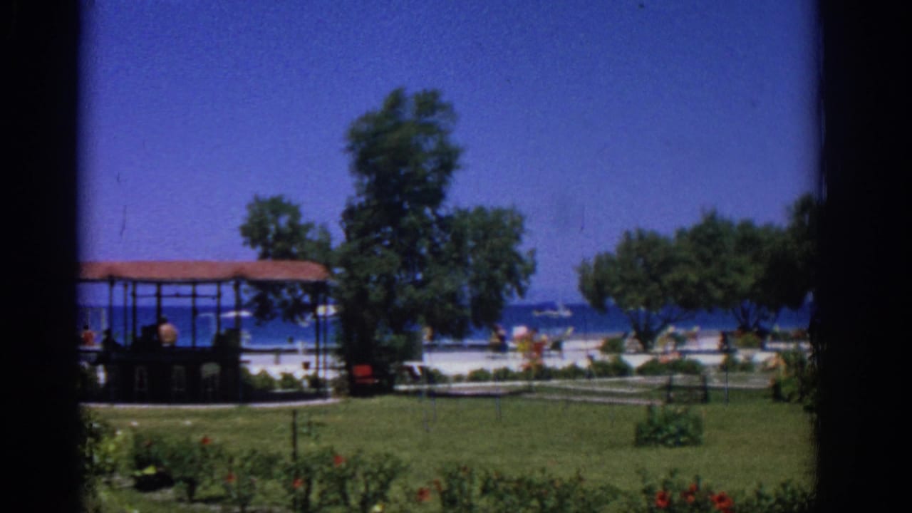 Garden lawn with trees, shaded structure, beach, and blue sea beyond.