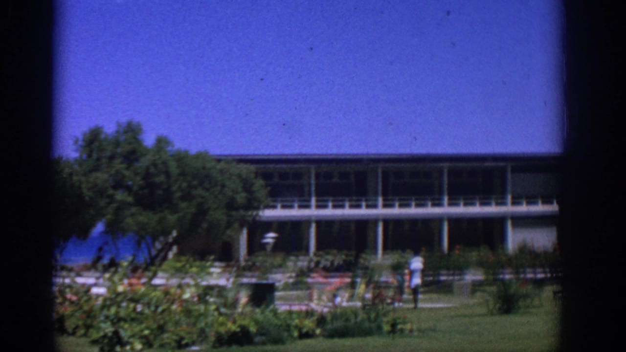 Garden in front of a two-story building with white columns and a small person near the center.