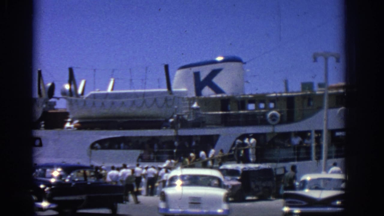Crowded quay with period cars beside a white ferry bearing a large K on its funnel.