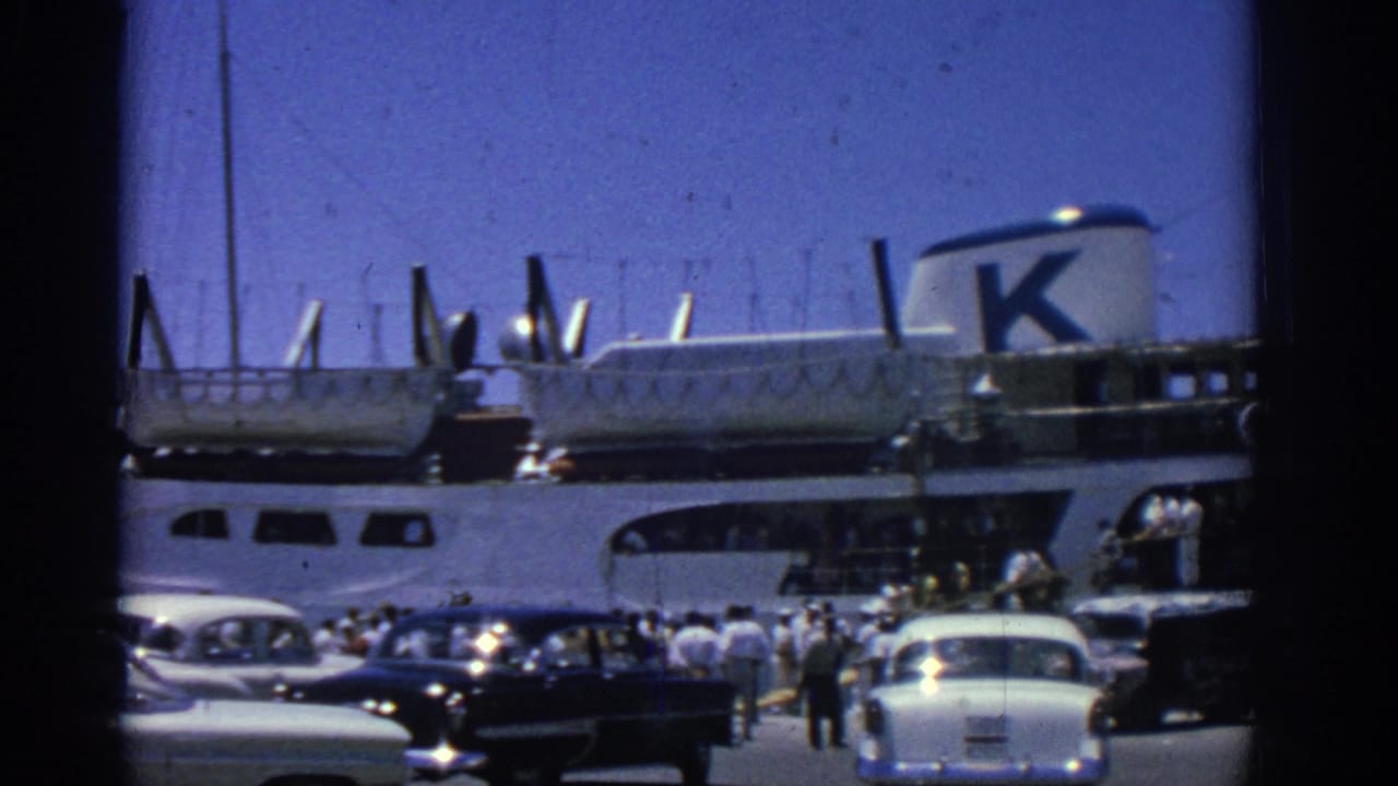 Rhodes harbor ferry scene from 1962, showing passengers near the dock, several period cars, and the ship's upper decks.