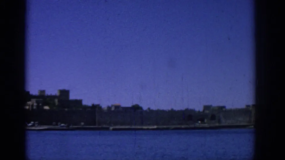 Rhodes, Greece, 1962 wide waterfront view across the harbor toward distant city walls under a clear blue sky.