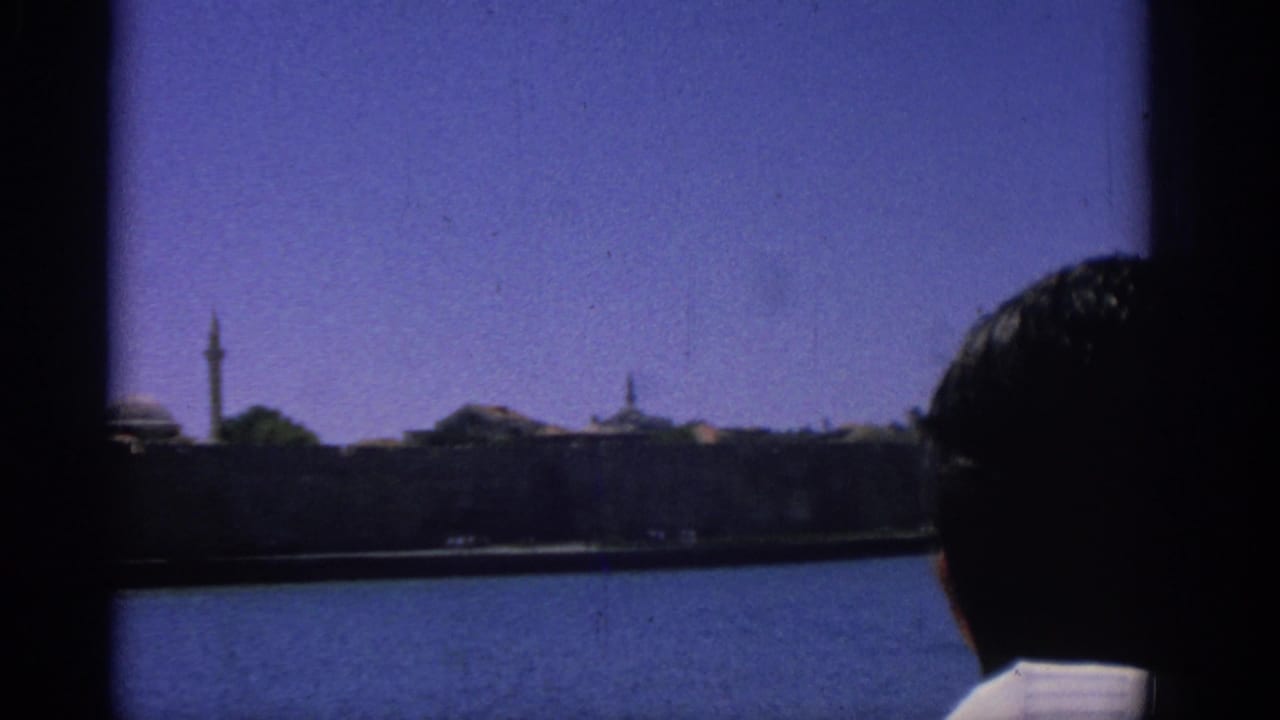 1962 Rhodes travel footage shows a silhouetted passenger facing the waterfront skyline from a moving boat.