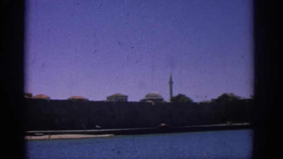 The Rhodes waterfront remains in view from the boat, with low buildings, a tower, and deep blue water in the foreground.