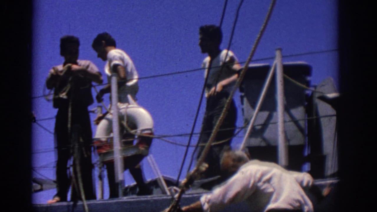 Sailors and crew stand on a boat deck among ropes and railings under a blue sky.