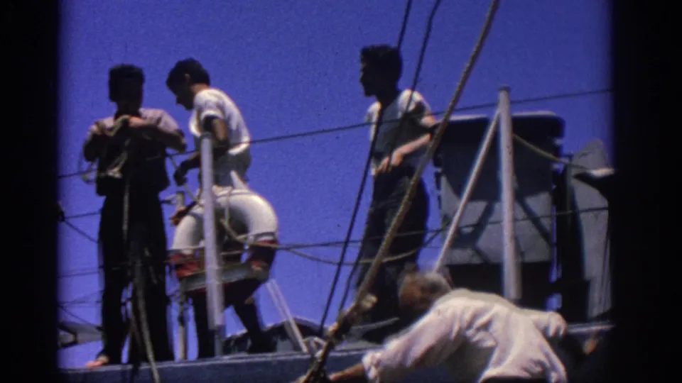 1962 Rhodes, Greece 8mm frame showing men on a boat deck with rigging, railings, and a mounted life preserver.