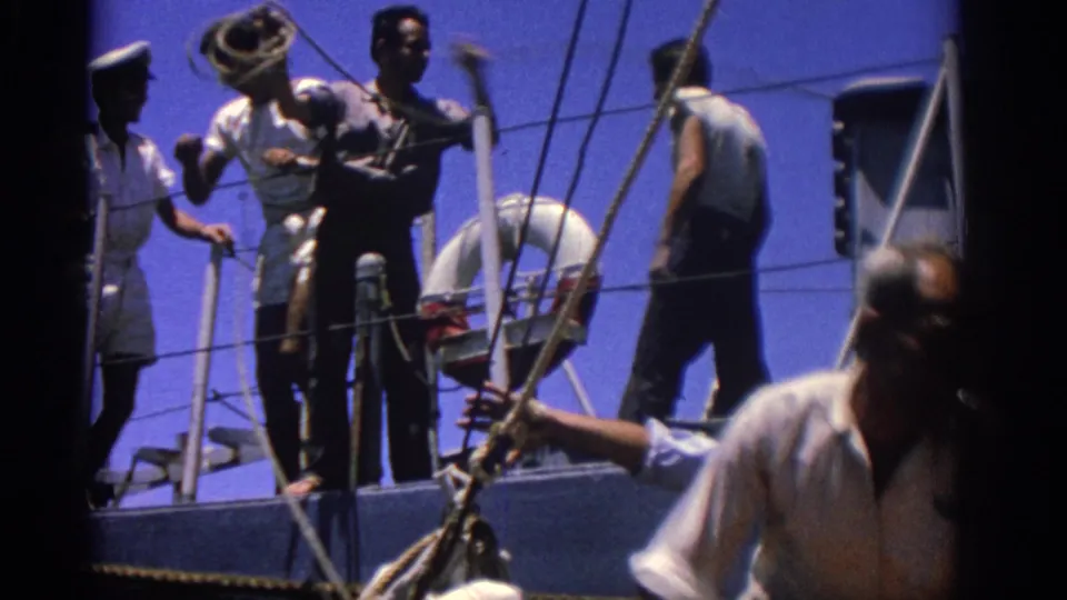 1962 Rhodes, Greece frame with sailors and crew handling deck equipment beside rigging and a life preserver.