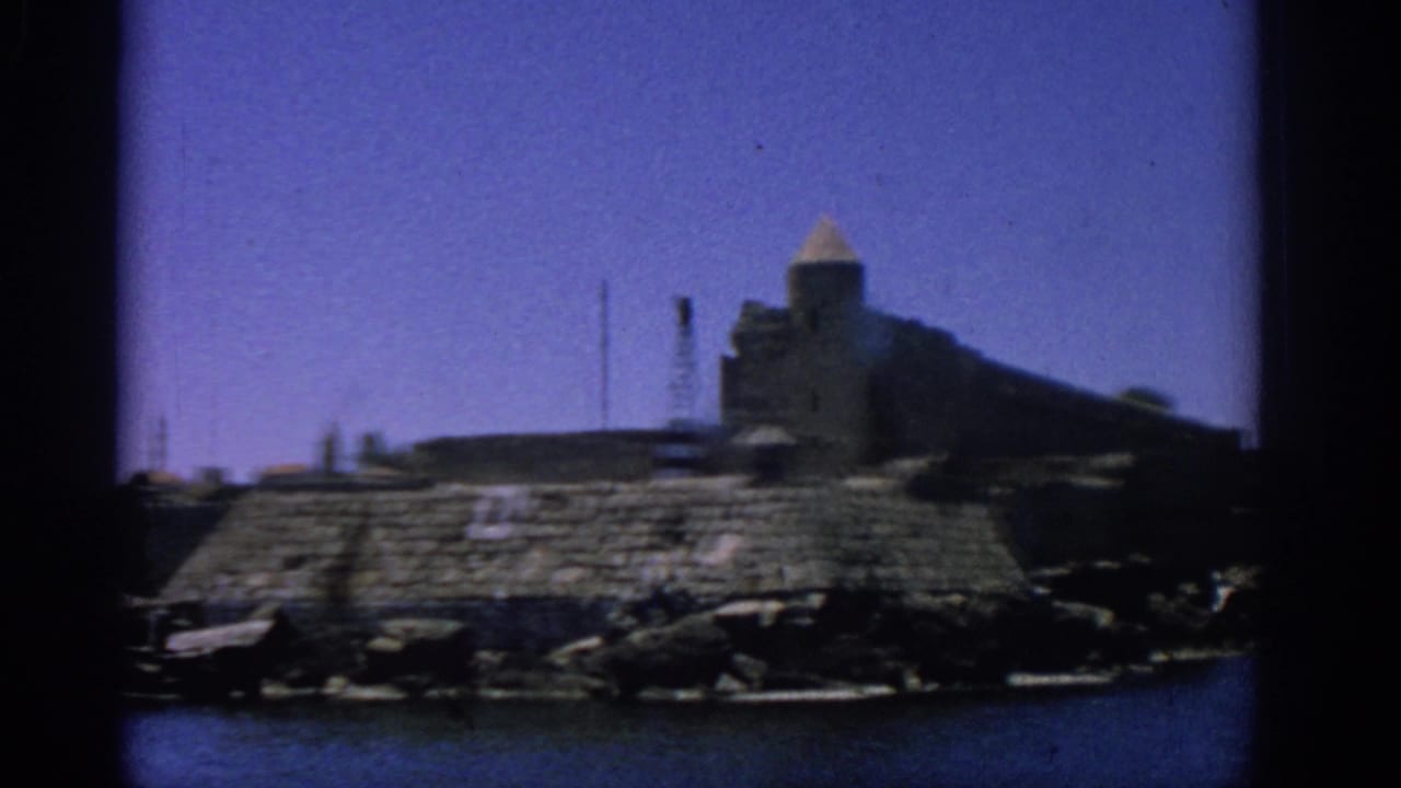 Stone fortress and tower on a rocky shoreline across blue water.