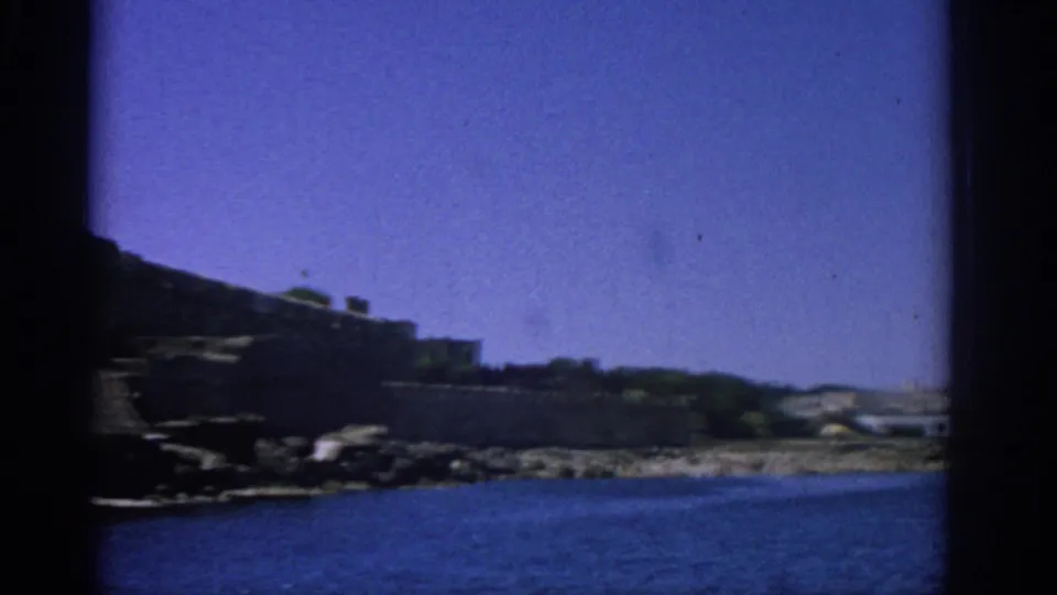 Visitor-shot 8mm frame showing the fortress edge, rocky shore and blue water in Rhodes in 1962.