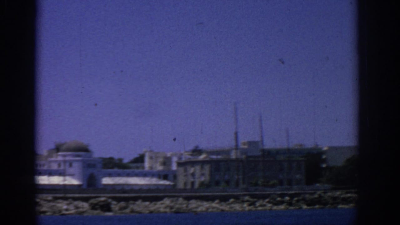 Waterfront buildings along a rocky shoreline under a deep blue sky.