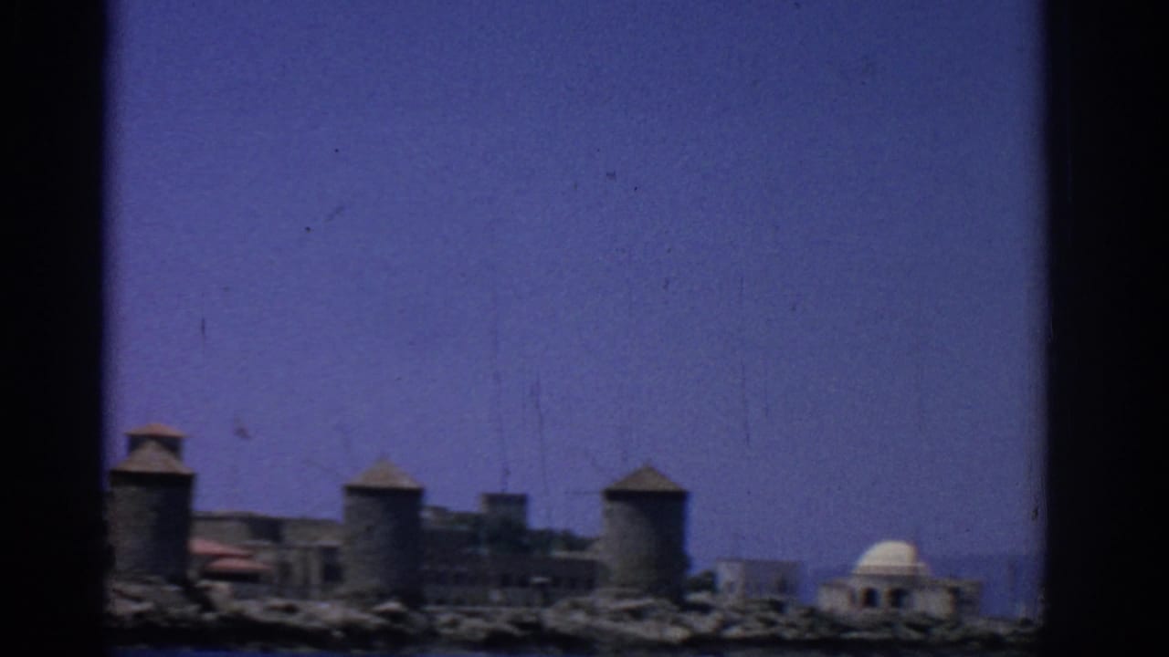 Historic waterfront with round towers and a pale domed structure near the shore.