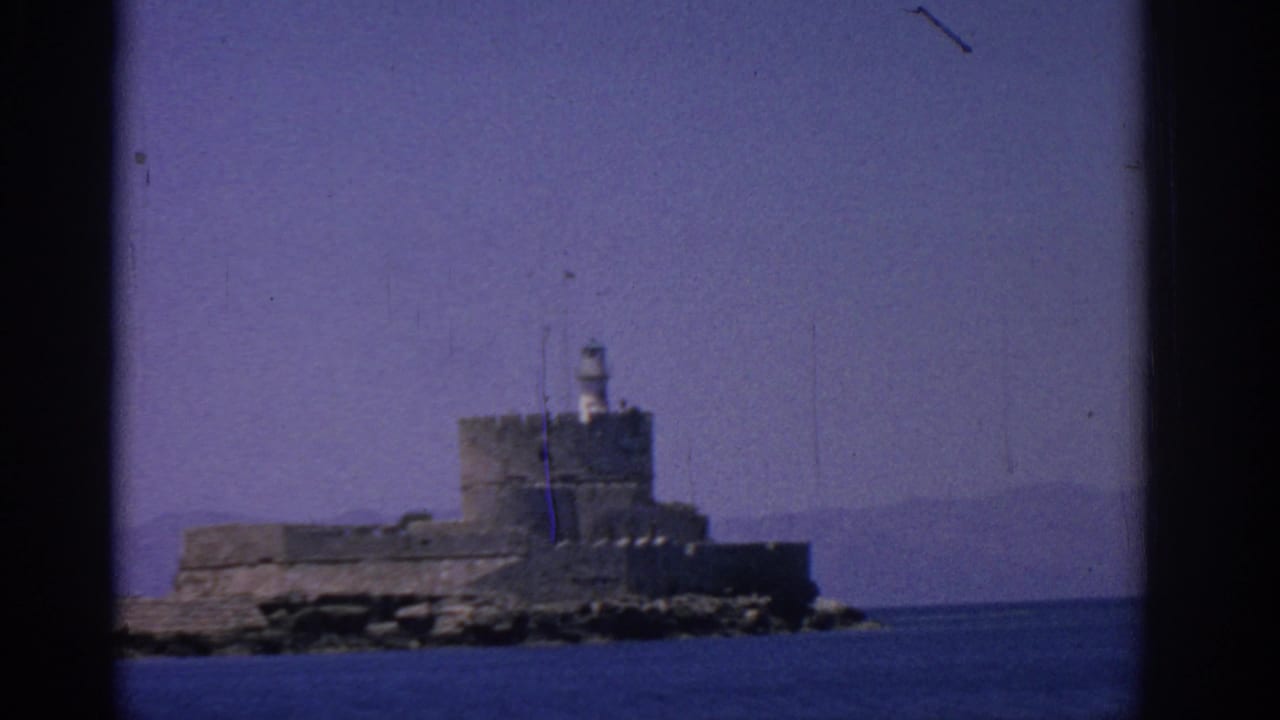Stone fortress and lighthouse framed by dark film borders over the sea.
