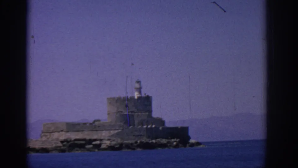 Distant Rhodes coastal fortress with lighthouse, blue water, and clear sky in 8mm archival color.