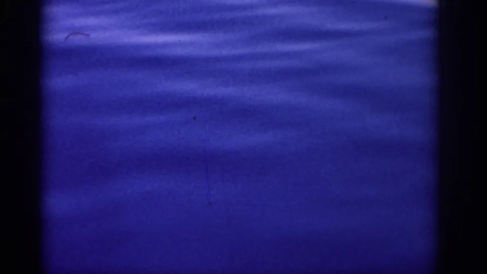 Blue-tinted 8mm view of the sea near Rhodes, with faint ripples, soft focus, and small physical-film marks.