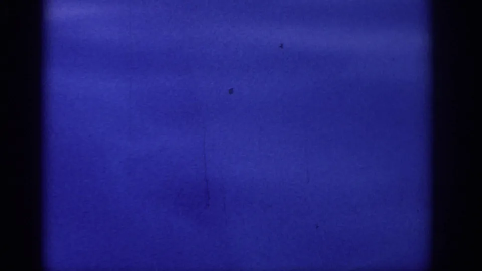 1962 8mm frame of blue sea surface in Rhodes, with a dark film edge, subtle tonal variation, and scattered specks.