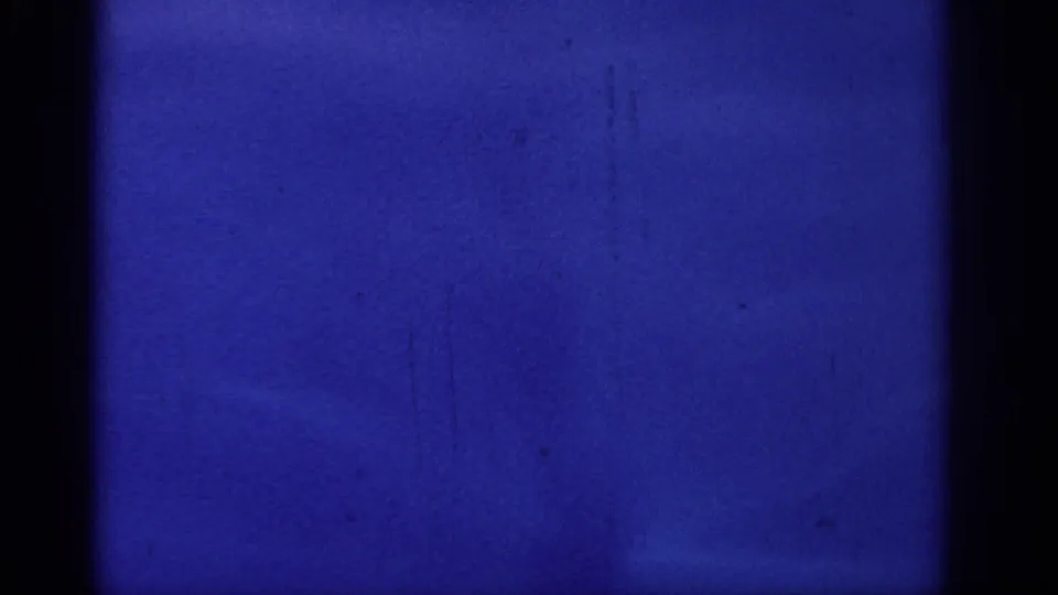 Blue 8mm film frame from the Rhodes home movie, showing gate edges, grain, and faint marks before the deck view appears.