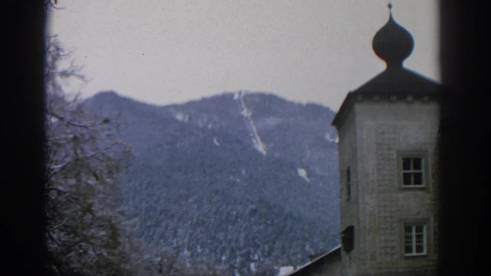 Munich, Germany 8mm frame with a tower at the right edge and a snow-streaked forested mountain ridge in the background.