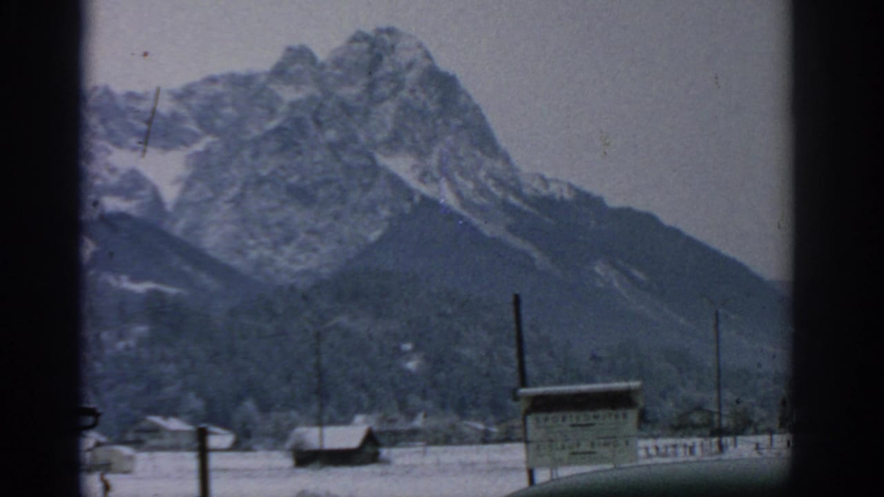Snowy alpine peak behind a village sign and utility poles.