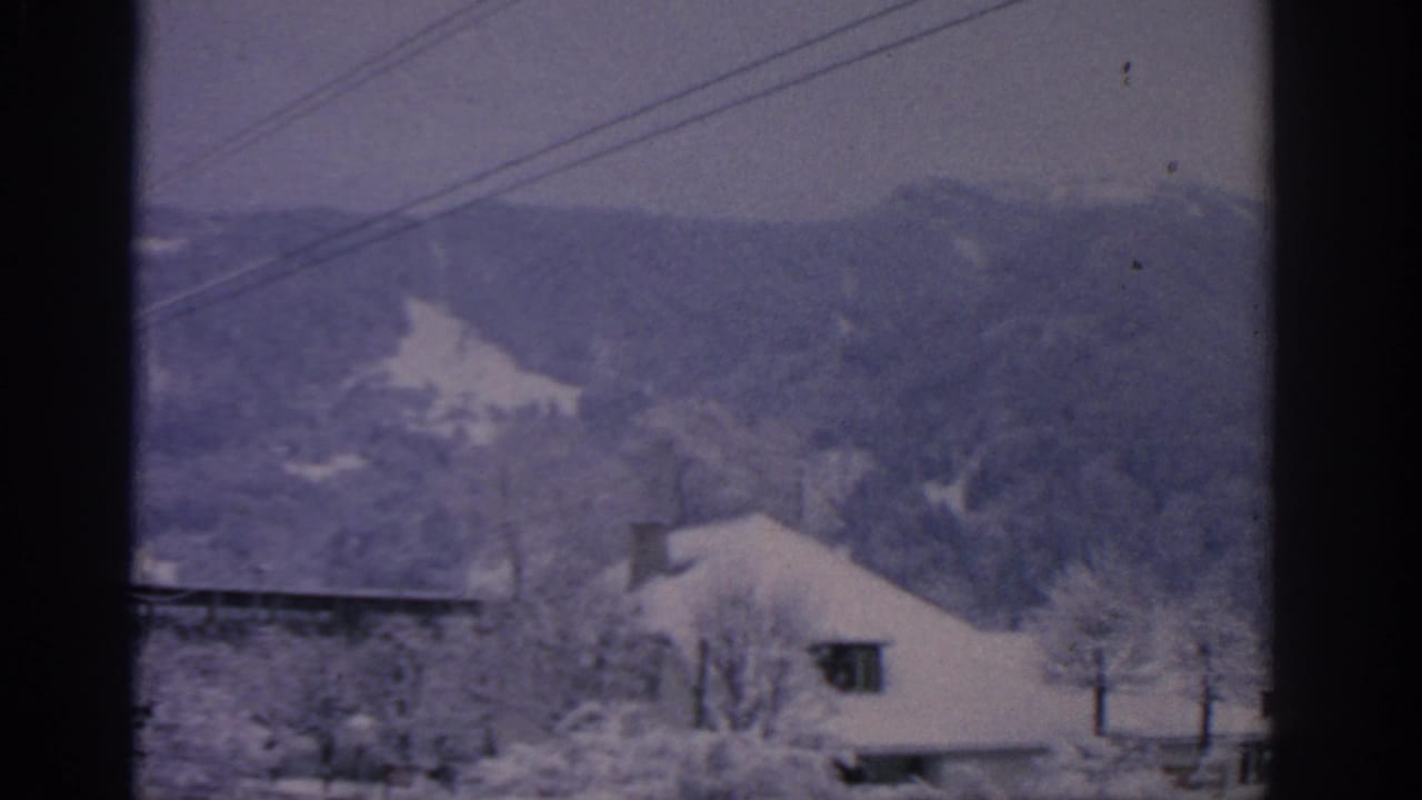 Snowy mountain landscape with a roofline, bare trees, and overhead cables.