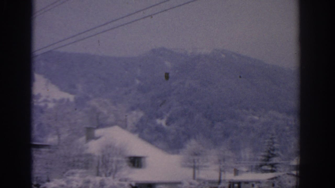 Snowy mountain slope behind a roofline and utility cables.
