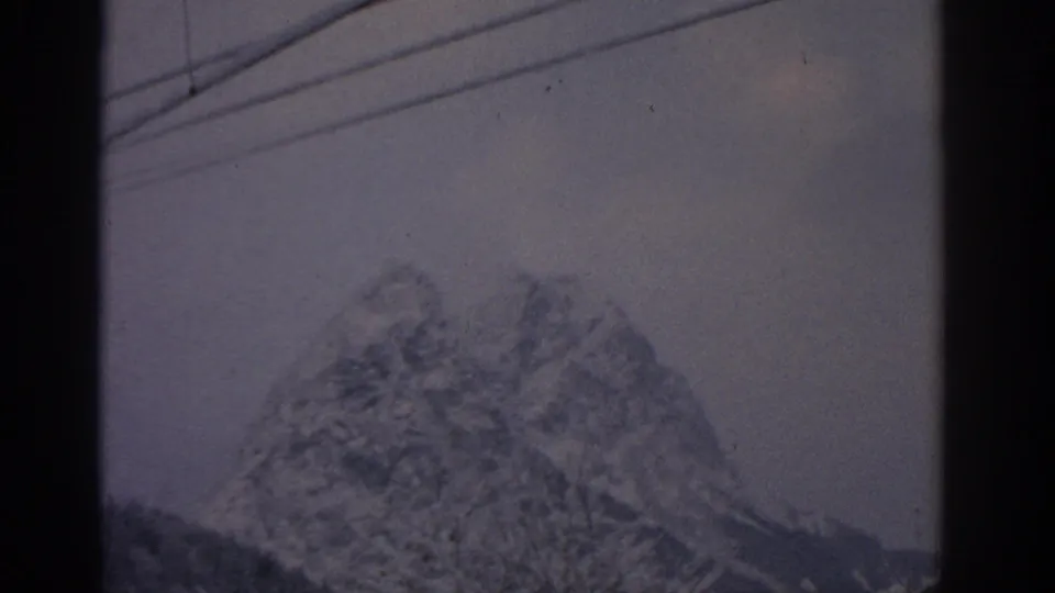 1963 German alpine view of a rugged snow-covered mountain peak seen below overhead lines and winter sky.
