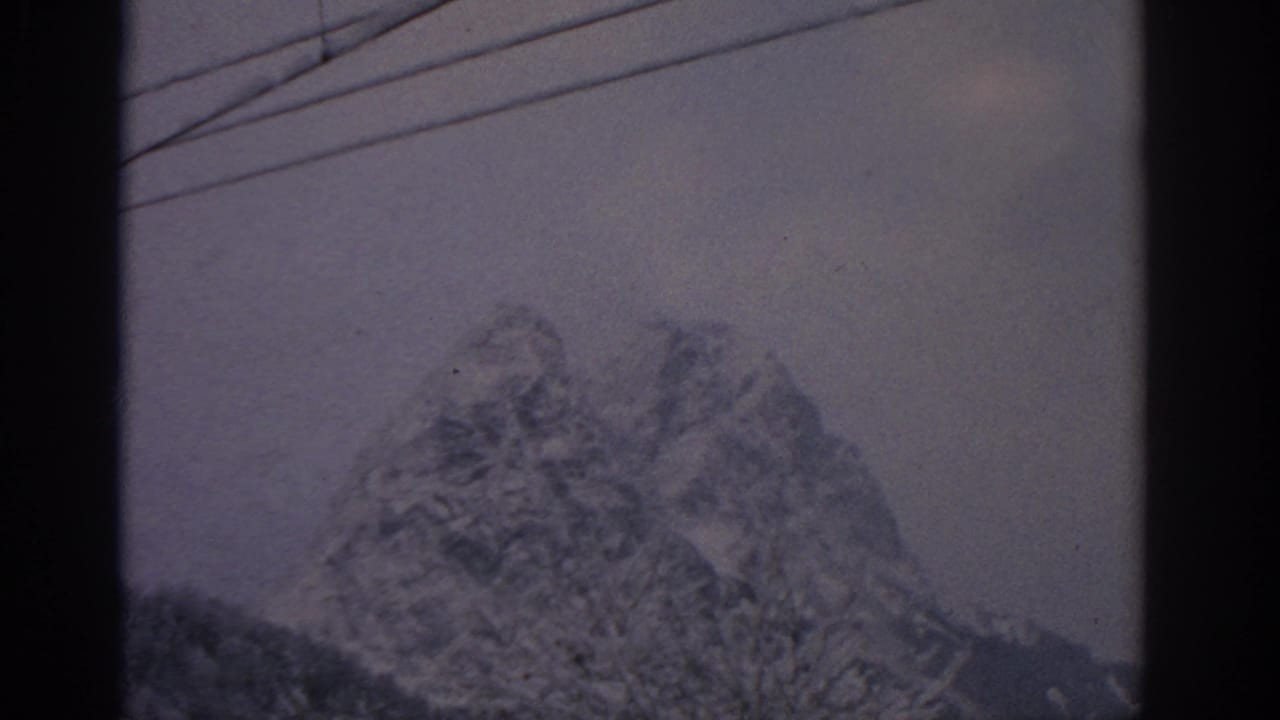 Snow-covered mountain under a cloudy sky with telephone wires across the upper frame.