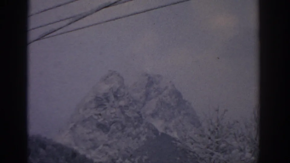 1963 8mm travel frame showing a soft, snow-dusted mountain view near Munich with telephone wires crossing the sky.