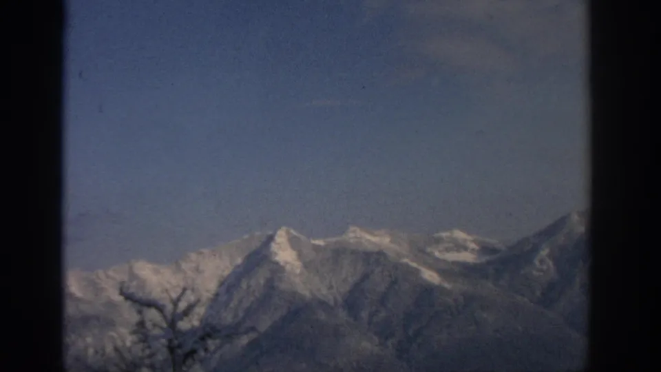 Clear 1963 alpine view near Munich with snow-covered peaks rising against a blue sky and visible 8mm film borders.