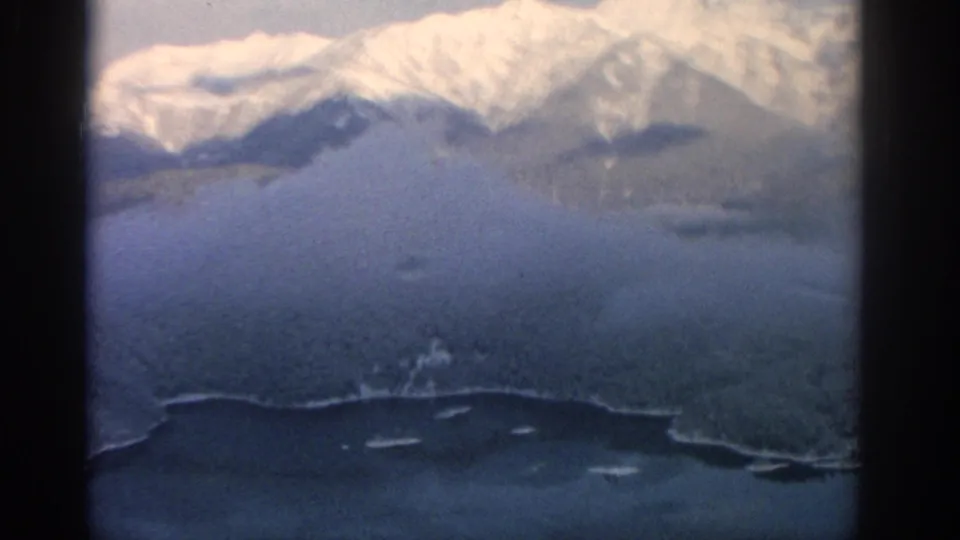 1963 Munich-area winter landscape with bright snowy peaks, lower dark terrain, and a lake or valley in the foreground.