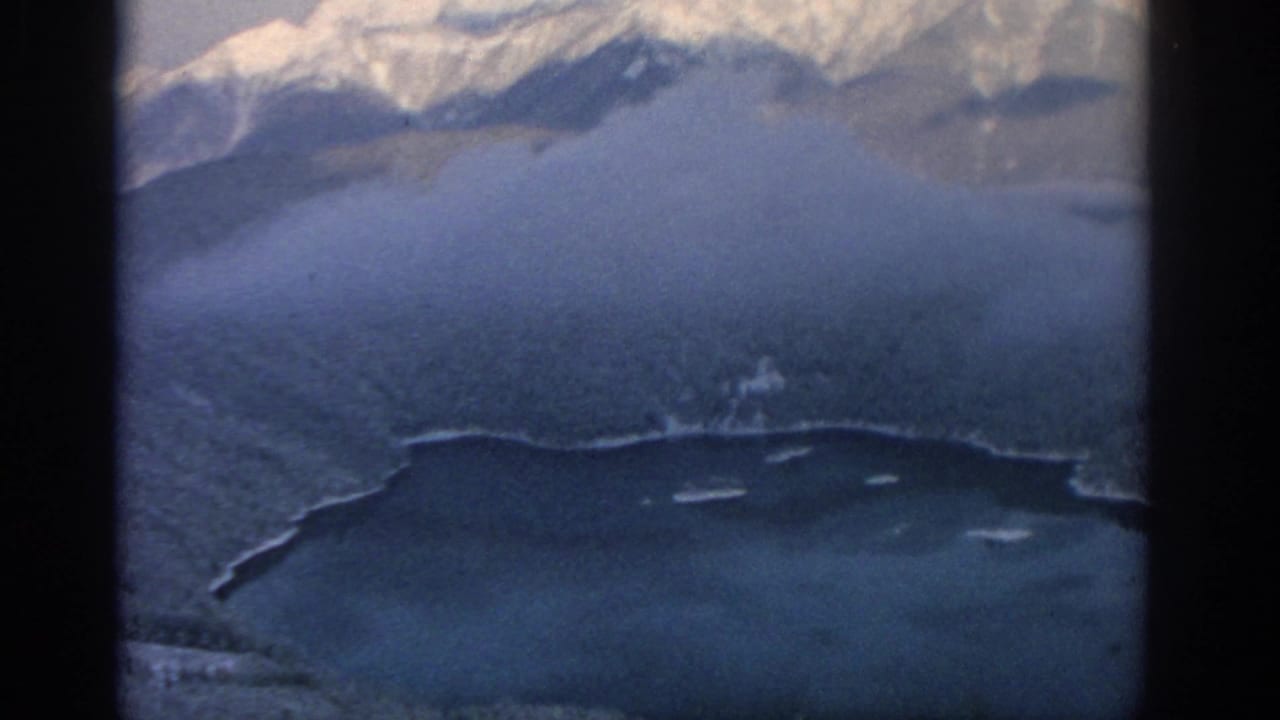 Aerial view of snowy peaks, forested hillside, and lakeside shoreline.