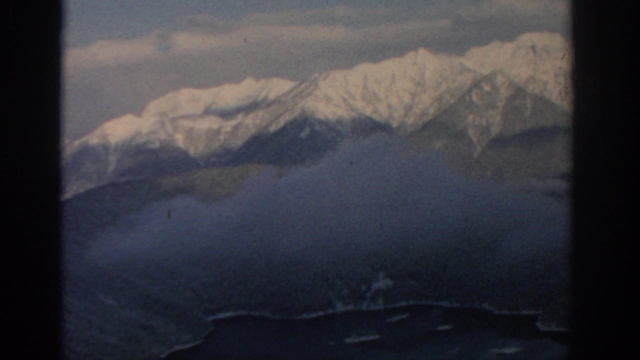 Snowy mountain ridge above dark forest and a lake, seen through 8mm frame edges.