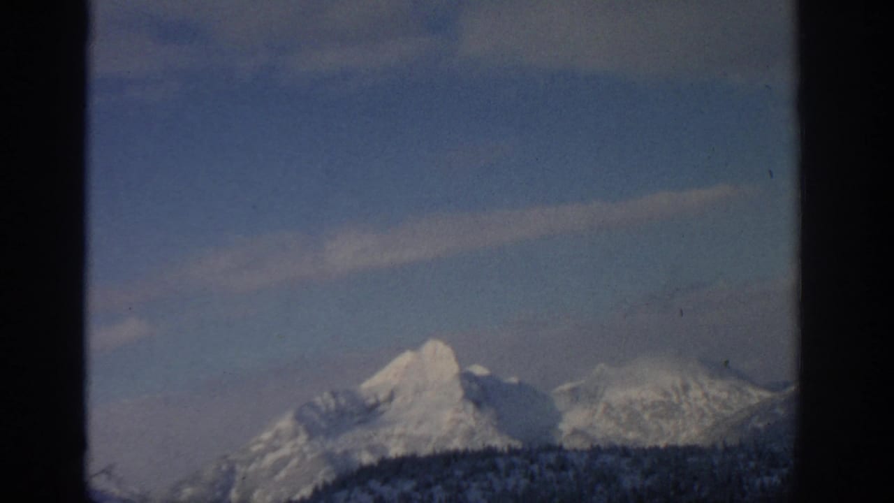 Distant snow-covered mountain range beneath a pale sky with dark film edges.