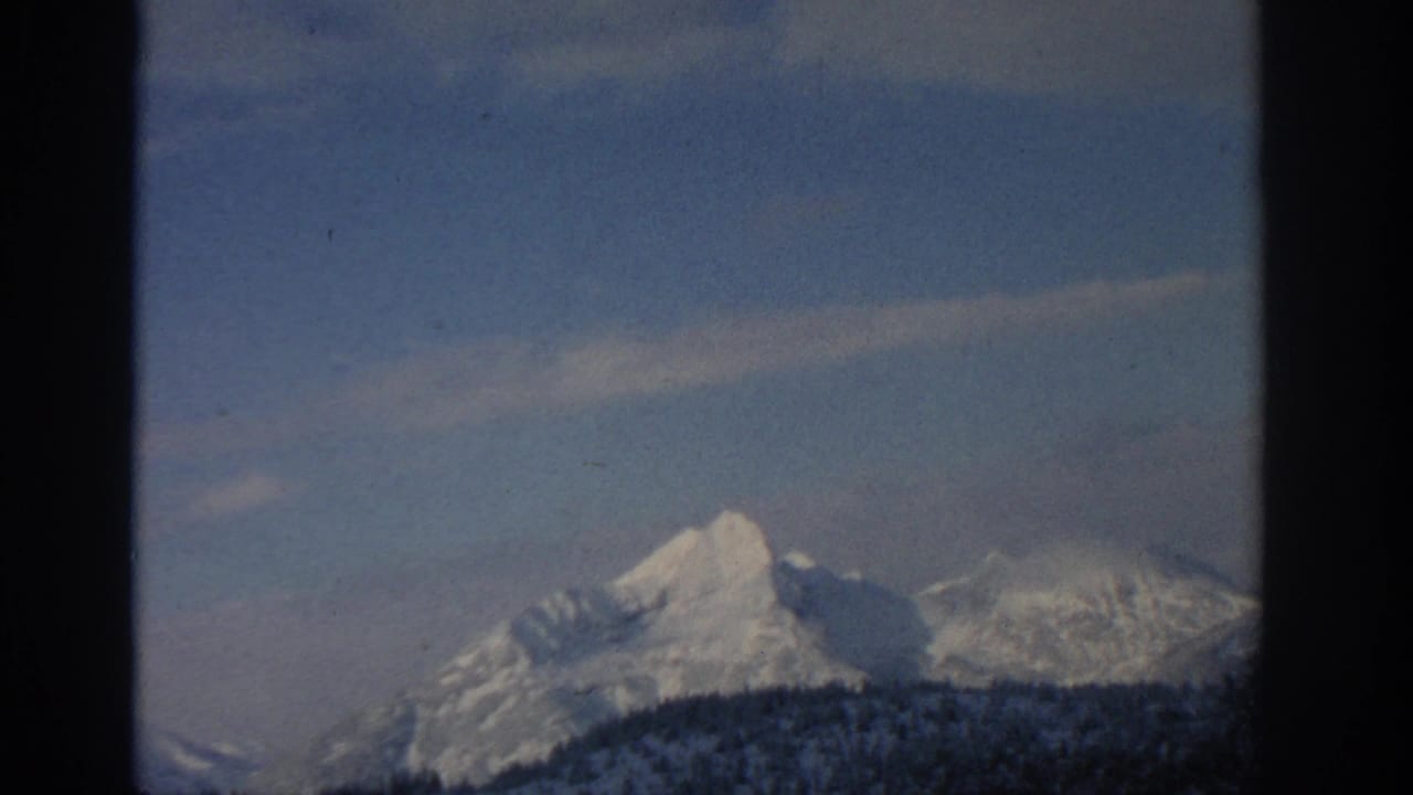 Snow-covered mountain peaks under a pale blue sky, framed by dark film edges.